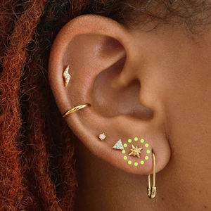 Detailed close-up of a model wearing a gold ear piercing set with opal and zircon