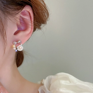 Close-up of pearl flower earrings with rhinestones and ribbon detail on a female model