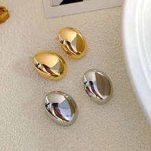 Macro view of polished oval pebble-shaped stud earrings in gold and silver finish