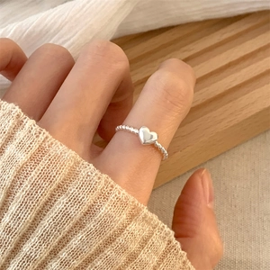 Close-up of a 925 silver heart ring with a beaded band on a woman's finger