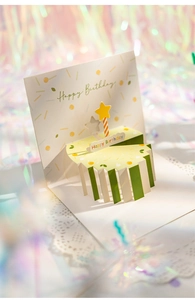 Macro detail of a 3D pop-up birthday cake card featuring a star candle and bokeh background