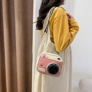 Pink and cream camera-shaped crossbody bag with chain strap worn by a model in warm light