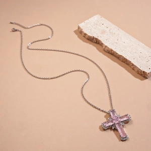 Collier croix en argent avec zircons roses sur un fond beige minimaliste épuré