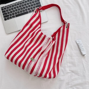 Détail du sac cabas en toile à rayures rouges avec bordure en dentelle blanche et logo métal