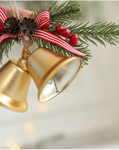 Nahaufnahme goldener Weihnachtsglocken mit Tannenzweigen, roten Beeren und Bandschleife