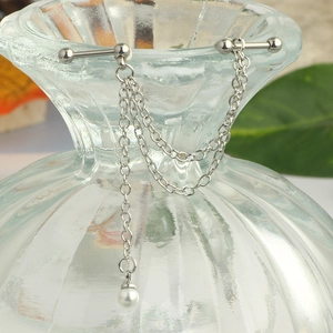 Detail of silver chain earring with star stud and white pearl drop on glass vase