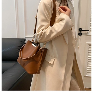 Close-up of a brown leather bucket bag styled with a beige coat for an elegant commute look