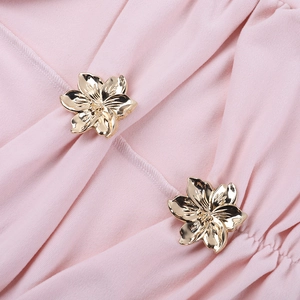 Dettaglio macro di fibbie metalliche a fiore dorato su tessuto di abito rosa