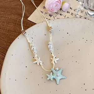 Détail d'un collier de plage avec pendentifs étoile de mer bleue, perles et coquillages