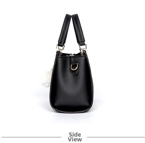 Side view of black faux leather handbag with elegant white fur ball charm and D-rings