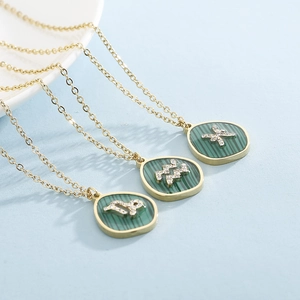 Detail of three gold zodiac necklaces with green malachite pendants and crystal symbols