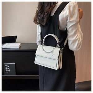 Detailed view of white PU leather crossbody bag with silver chain and top handle on a table