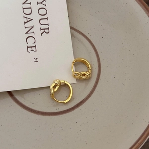 Detailed view of gold knotted hoop earrings on a minimalist ceramic jewelry plate