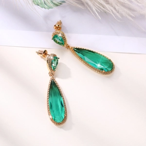 Macro shot of long emerald teardrop earrings with gold setting and white crystal accents
