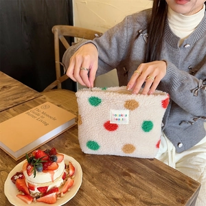 Close-up of colorful polka dot plush makeup bag with woven label on a wooden desk