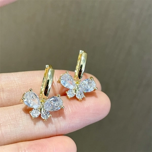 Close-up of golden butterfly earrings with sparkling cubic zirconia on a person's finger