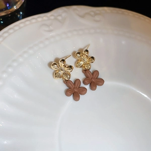 Detailed close-up of brown matte double flower earrings with golden metal accents on white tray