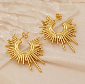Detail of gold sunburst semi-circle earrings on cream textured fabric backdrop