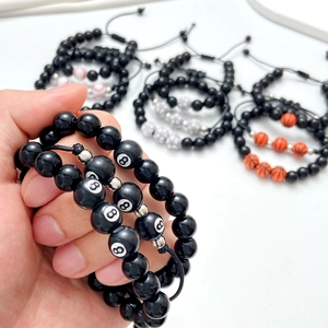 Detail eines verstellbaren Perlenarmbands mit 8-Ball und Sportmotiven am Handgelenk