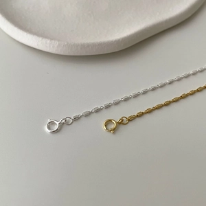 Detail of silver and gold square link chains on a minimalist ceramic plate background