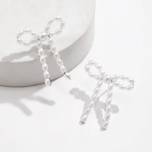 Detail of elegant bow earrings crafted with woven white faux pearls on a stone display