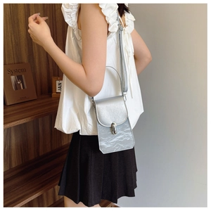 Close-up of silver textured crossbody phone bag with metal lock worn by a model