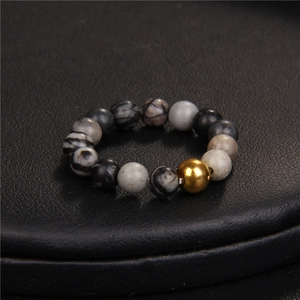 Beaded ring with natural grey marble stones and an 18K gold bead on black leather surface