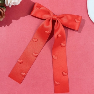 Detail of red satin bow hair clip with textured hearts and long elegant streamers