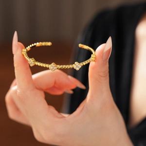 Dettaglio ravvicinato di un bracciale rigido in oro 18k con ciondoli a quadrifoglio e zirconi