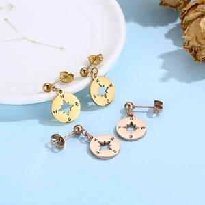 Détail de boucles d'oreilles boussole en or 18k et or rose sur un fond bleu pastel