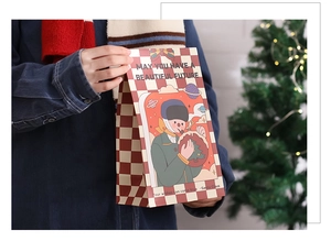 Detail of hand holding a festive red checkered Christmas gift bag with holiday illustration