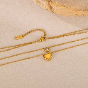 Detail of a gold double-layer stainless steel necklace with heart and crystal pendants