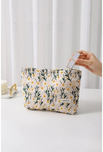 Detailaufnahme einer Hand, die Lippenstift in eine bestickte Baumwollkosmetiktasche legt