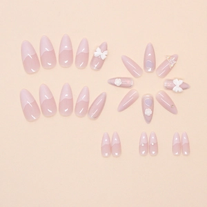 Detail of pink almond press-on nails with 3D white bows, flowers, and sparkling rhinestones