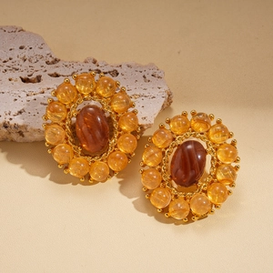 Detalle de pendientes vintage dorados con ágata ámbar sobre una base de piedra natural beige