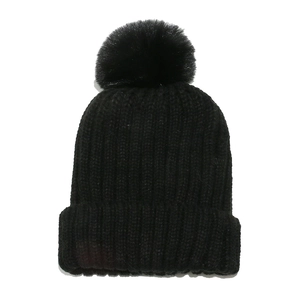 Close-up of black ribbed knit beanie with soft faux fur pom-pom and thick winter texture