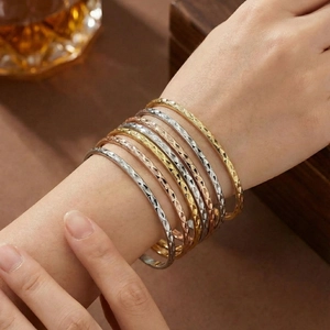 Close-up of stacked geometric diamond pattern bangles in gold, silver and rose gold