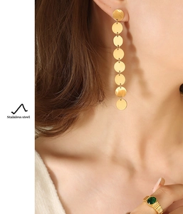 Close-up of golden sequin drop earrings and emerald gemstone ring in stainless steel