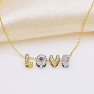 Detailed close-up of gold LOVE pendant necklace with cubic zirconia on silk background