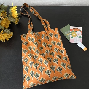 Flat lay of floral canvas tote bag with orange leaf pattern on a rustic wooden background