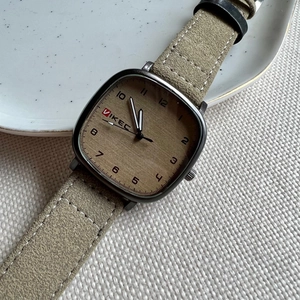 Detail of square wood grain dial and beige suede strap on a neutral quartz watch