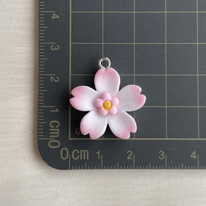 Pink cherry blossom resin pendant with silver ring shown on a centimeter scale mat