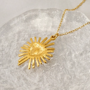 Collier avec pendentif cœur soleil doré posé sur une surface en verre dépoli