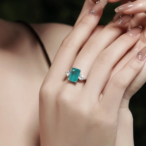 Detail of emerald cut green gemstone ring with side stones on a model's finger