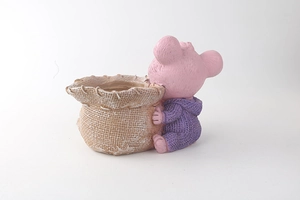 Dettaglio di orsetto in resina rosa con maglione viola che tiene un vaso a forma di sacco