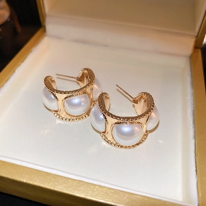 Détails de boucles d'oreilles perles dorées en C style rétro français sur un écrin beige