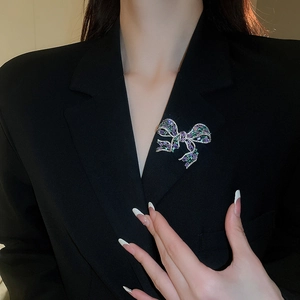 Close-up of a bow brooch with purple and green crystals on a black suit jacket