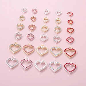Macro detail of mixed heart charms with crystals and pearls on soft pink background
