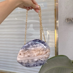 Detail of egg-shaped marble pattern clutch bag with gold chain and glossy purple finish