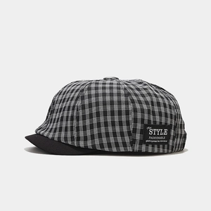 Detail of checkered newsboy hat featuring a side fabric patch and textured black brim